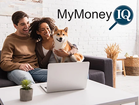 couple with dog in their lap smiling looking at laptop in home