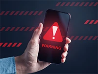 Hand holding smartphone displaying red warning alert symbol
