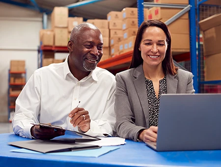 Two employees working in a warehouse on a laptop